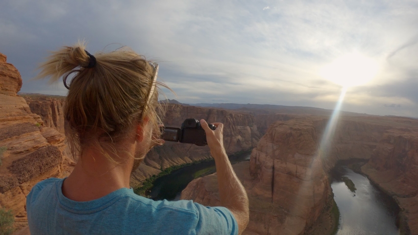 Male photographer takes photos at famous Horseshoe Bend lookout in Page, Arizona. Man tourist travelling in USA taking picture of stunning canyon river bank from above