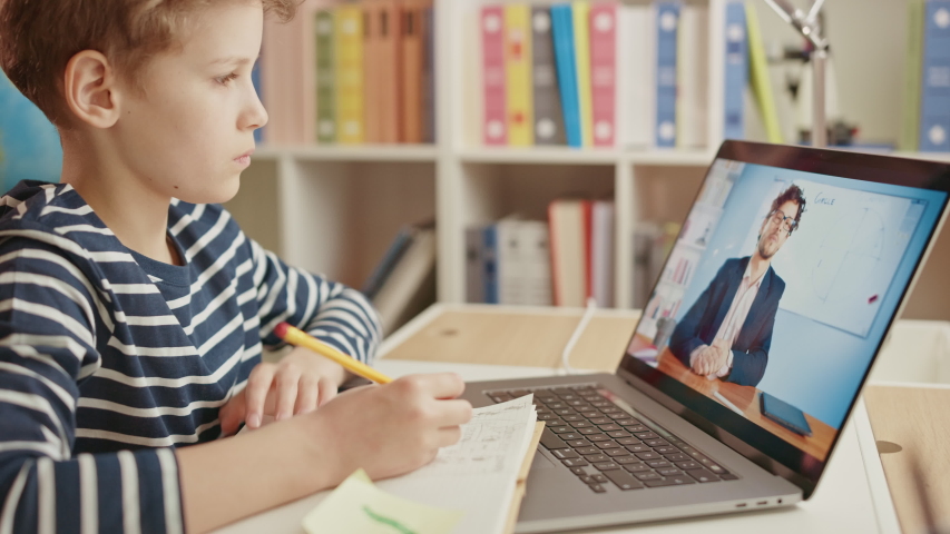 Smart Little Boy Uses Laptop for Video Call with His Teacher. Screen Shows Online Lecture with Teacher Explaining Subject from a Classroom, Boy writes Down Information. E-Education Distance Learning Royalty-Free Stock Footage #1052644124