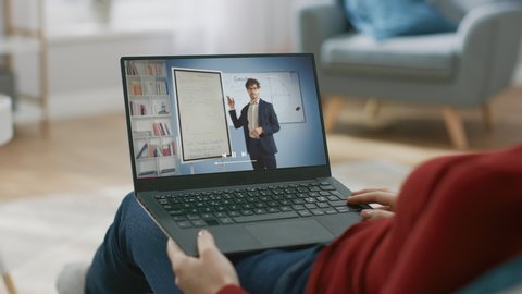E-Education, Online Courses: Woman Sitting on a Couch Uses Laptop to Watch Internet Lecture on Business, Screen shows Professional Business Coach Talking about e-Commerce, Marketing, Uses Whiteboard