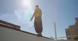 Caucasian man, wearing casual clothes, practicing parkour on a rooftop in a city on a sunny day, doing a somersault and holding a flare, with another man standing in the background, in slow motion. - Powered by Shutterstock - Get 15% off with code: PIKWIZARD15