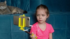 Little girl with a selfie stick takes pictures on the phone at home.