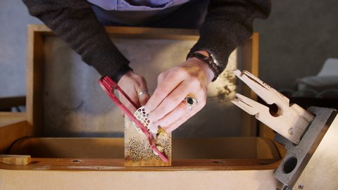 Overhead close up of female jeweller working on brooch in studio with saw - shot in slow motion