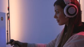 The smiling gamer girl with headphones plays video game in the blue light studio