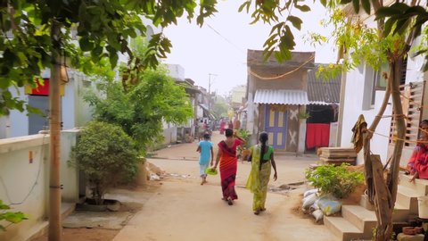 Yeleswaram , Andhra Pradesh / India - 11 02 2019: Tracking shot along late afternoon narrow tree lined Indian village street following three sari-wearing women walking away from camera