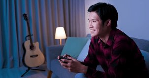 asian man use gamepad and play video games happily in the evening at home