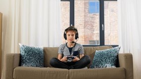 leisure, children, technology and people concept - boy in headphones with microphone and gamepad playing video game at home