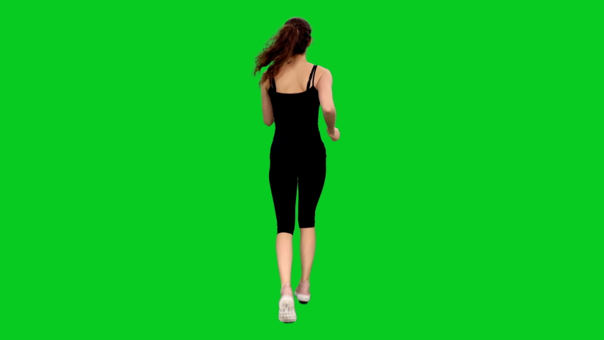 Rear view of slim young sporty woman jogging against green screen background, Full body chroma key 4k footage