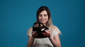 young blonde woman in white t-shirt puts on orange virtual reality headset to play video games on blue background slow motion