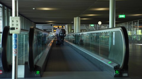 Schiphol Airport, Netherlands - May 9 2020: Two people walking on the travelator, moving walkway at the empty Amsterdam Schiphol Airport during social distancing, travel ban due to corona COVID-19 