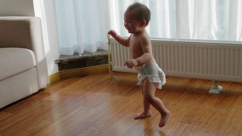 Baby asian girl just learning to walk at home slow motion of topless Chinese baby walking to her grandmother by the window senior Chinese woman with her granddaughter lifestyles indoor