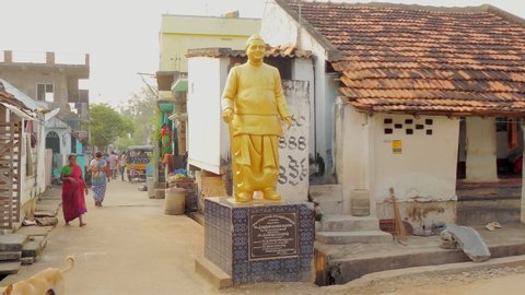 Yeleswaram , Andhra Pradesh / India - 11 02 2019: Barefooted, sari-wearing Indian village woman walks along Indian village street past golden statue of Dalit leader and 4th Deputy Prime minister of In