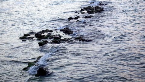Sea wave gently washing a stone reef on the coast