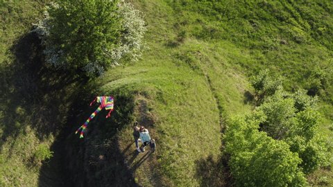 Top view of a young mother with her children plays with a kite on amazing green hilly terrain, aerial view