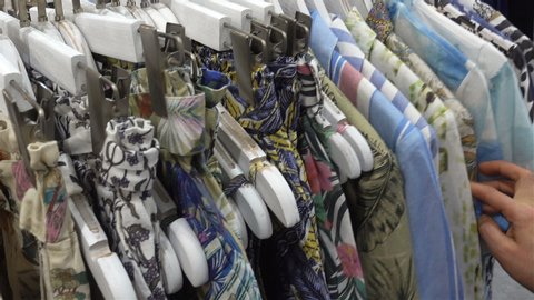 Female hand chooses colorful summer clothes on hangers in a store