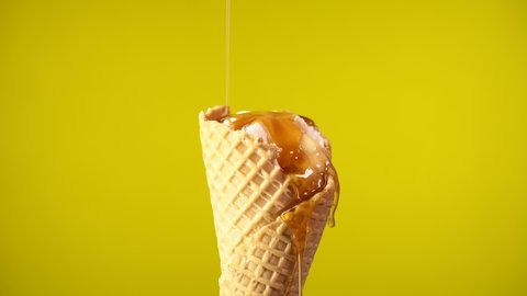 Ice Cream Horn in Waffle Cup on which Yellow Syrup, Maple Syrup is Poured. Yellow Background, 4K. Close-Up footage of delicious dessert. Ideal for food and recipe videos.