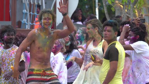 HOLI FESTIVAL OF COLOURS, MALDIVES HIMMAFUSHI, AUGUST 2019: CLOSE UP: Cheerful young tourists point and look into the camera while dancing at a Holi festival taking place in the picturesque Maldives.