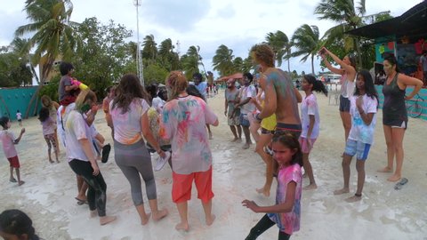 HOLI FESTIVAL OF COLOURS, MALDIVES HIMMAFUSHI, AUGUST 2019: CLOSE UP: Joyful locals of the Maldives and travelers celebrate the Holi festival on a rainy day. Happy people dance on the sandy beach.