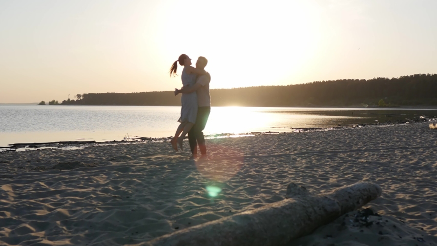 Romantic couple running on beach at sea sunset holding hands and jumping in slow motion. Man takes woman in air and turning her around. Concept of love and happiness