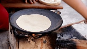 Indian Roti or Indian flatbread being kneaded with rolling pin.woman flatting the dough to make roti in an Indian Chulah in a village home. Indian women preparing roti.