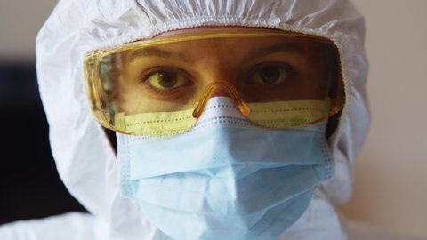 Portrait young female scientist look serious working in the laboratory wearing full body hazmat white protective suit for healthcare. Pandemic. Coronavirus.