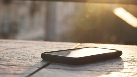 Black smartphone with blank screen holographic interface animated touchscreen lying on concrete surface floor balcony. Sunset flare. Innovation, technology.
