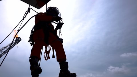 Working at height. Silhouette of abseiler team hanging at the edge oil and gas platform for maintenance works with background flare tip boom burning.