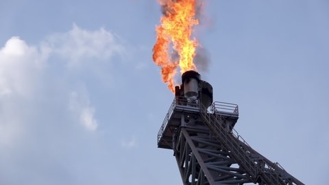 Oil and gas. Slow motion of gas flare from bottom burning at oil and gas platform with background blue sky and clouds.