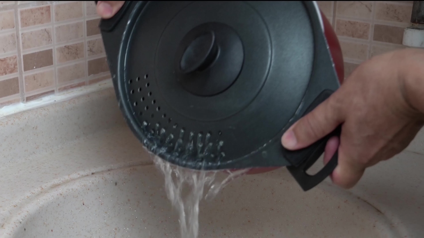 Hands pouring water from boiled pasta over sink in the kitchen.  Saucepan for pasta which its cover is also a strainer.
