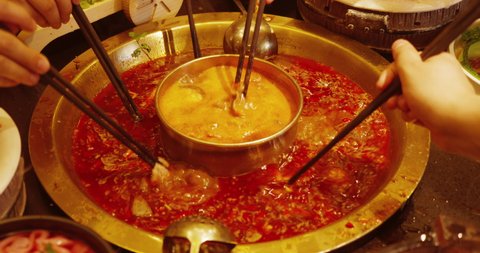 Close up of people eating together using Chopsticks putting vegetable and meat into the hotpot red spicy boiling soup Chinese Sichuan food
