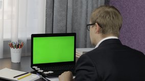 Male teacher looking at web camera making video call on laptop with green screen, chroma key. Working online from home. Distance education with children class on internet. Conference training webinar