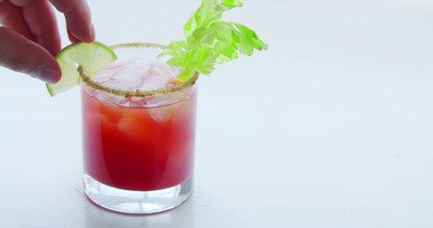A person making a caesar cocktail or bloody mary on a glass on a white background