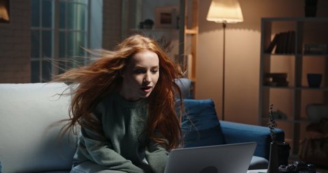 Pretty caucasian redhead girl looking at laptop screen, hair blowing, reading breaking news, seeing shocking discount during online shopping, vowing in amazement 4k footage