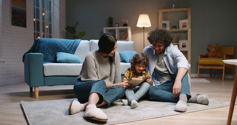 Cute young asian family spending time together at home. Little boy with curly hair reading a book with his parents, happily smiling - happy family, recreational pursuit concept 4k footage