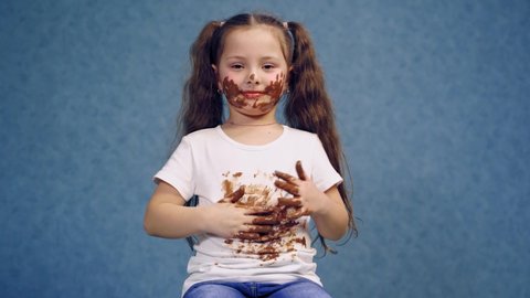 Portrait of dirty little girl after eating chocolate. Funny child with two ponytails have smeared face and white t-shirt in chocolate.
