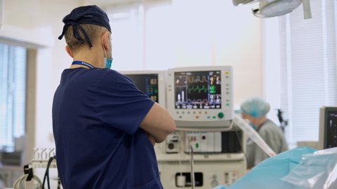 KYIV, UKRAINE - March 2020: Medical worker looking on the monitors during surgery. Screen of monitors showing vital signs of a patient. Modern operating theater in the hospital.