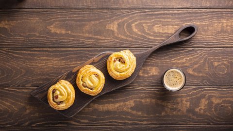 Stop motion animation of breakfast table setting with fresh pastry sweet swirl buns with raisins on wooden board. Top view, overheadshoot.