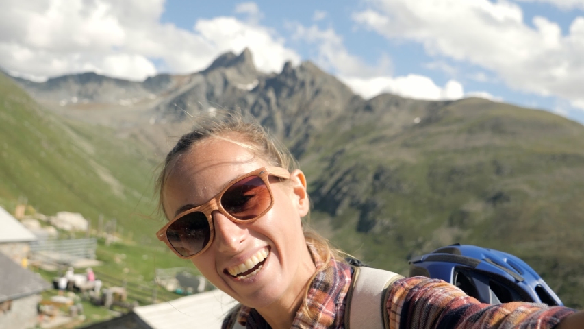 Woman hiking in the mountains takes a selfie portrait surrounded by nature. Solo traveller on social media 
