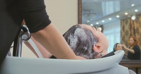 professional beauty salon worker washes young woman hair massaging shampoo on head over special sink close view