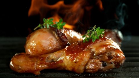 Super slow motion of chicken legs on grill with fire, on black background. Filmed on high speed cinema camera, 1000 fps