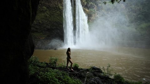 Silhouette of a Young Woman at a Waterfall (Wailua Falls) in Kauai, Hawaii. Tilt up, slow motion.
