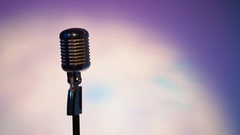 Professional silver vintage glare microphone for record or speak to audience on scene in dark empty retro club close up. Spotlights shine on a chrome mic with highlights on space fantastic background.