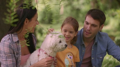 Beautiful happy family is having fun with bichon dog outdoors in the park
