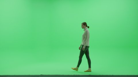 Green Screen Chroma Key Studio: Beautiful Young Woman Wearing Stylish Casual Clothes Walks Across Room Right to Left. Side View Camera Shot