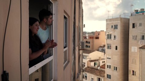 Young spanish couple giving an applause to all sanitary staff and kissing from her apartment window during quarantine from COVID 19 in Mallorca, Spain