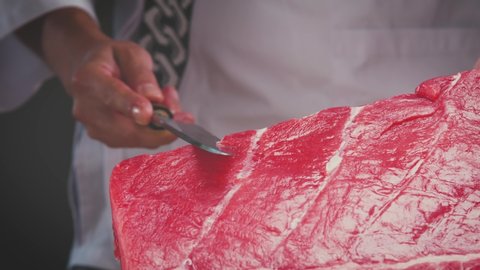 Slow motion closeup of anonymous cook slicing fresh tuna on white table while preparing healthy dish in kitchen