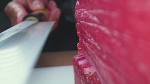 Zoom out view of anonymous cook slicing raw bluefin tuna flesh while preparing sashimi in traditional Japanese restaurant
