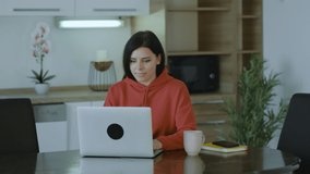 Excited brunette woman reading good news on notebook in home, looking at laptop celebrates online success at home. Feels motivated.
