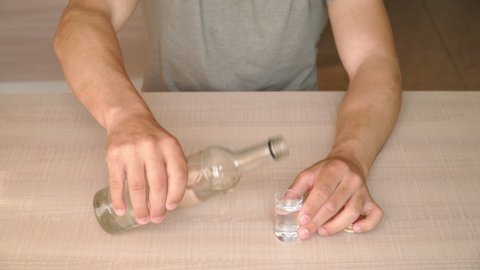 A young guy drunkard alone at home at the table drinking an alcoholic beverage. The concept of the problem of alcohol dependence. Drunkenness and bad habits.