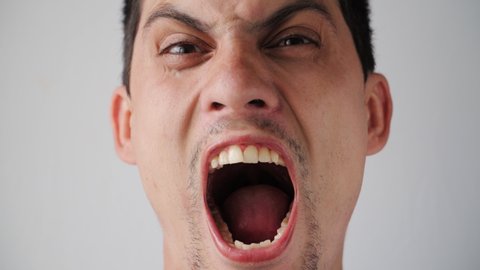 Portrait of Young Caucasian angry guy yells directly into the camera. Men's emotions on a white background. Slow motion. Close-up.