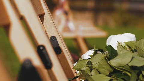 CU, slow motion: white fresh rose flower bouquet on stylish wooden chair with ribbons waved by wind at beautiful wedding venue on sunny day closeup